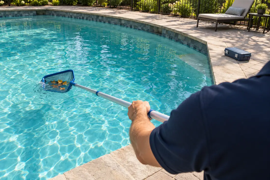 A technician skimming a backyard pool